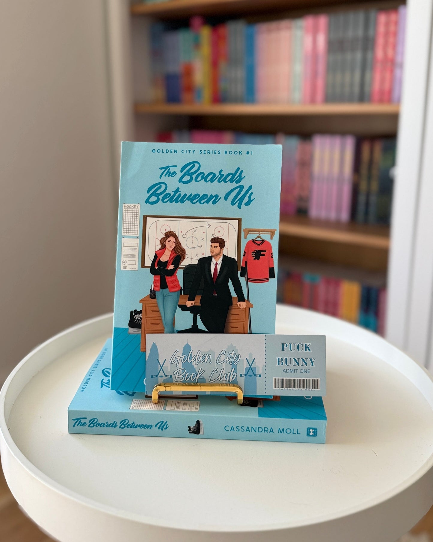 Book titled 'The Boards Between Us' on a white table with a bookshelf in the background