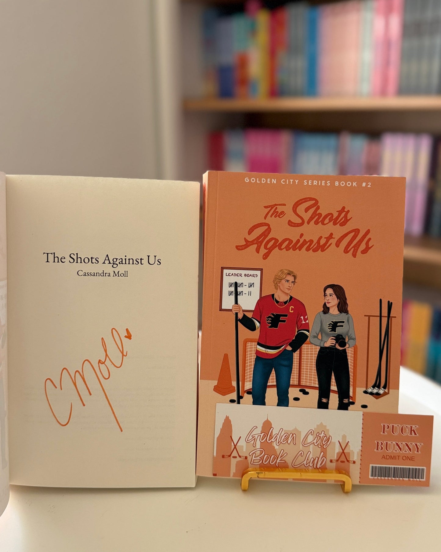 Book titled 'The Shots Against Us' on a surface with a blurred bookshelf in the background.