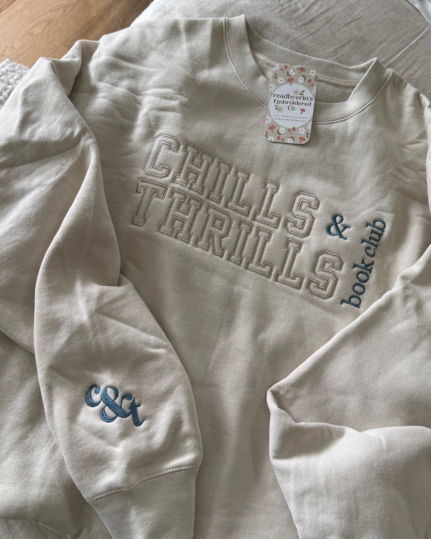 Beige sweatshirt with 'Chills & Thrills & Book Club' text on a bed