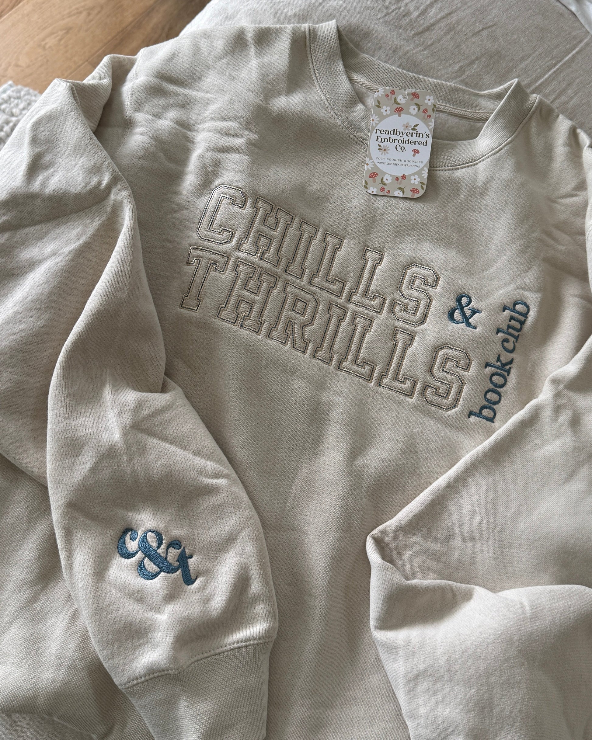Beige sweatshirt with 'Chills & Thrills & Book Club' text on a bed