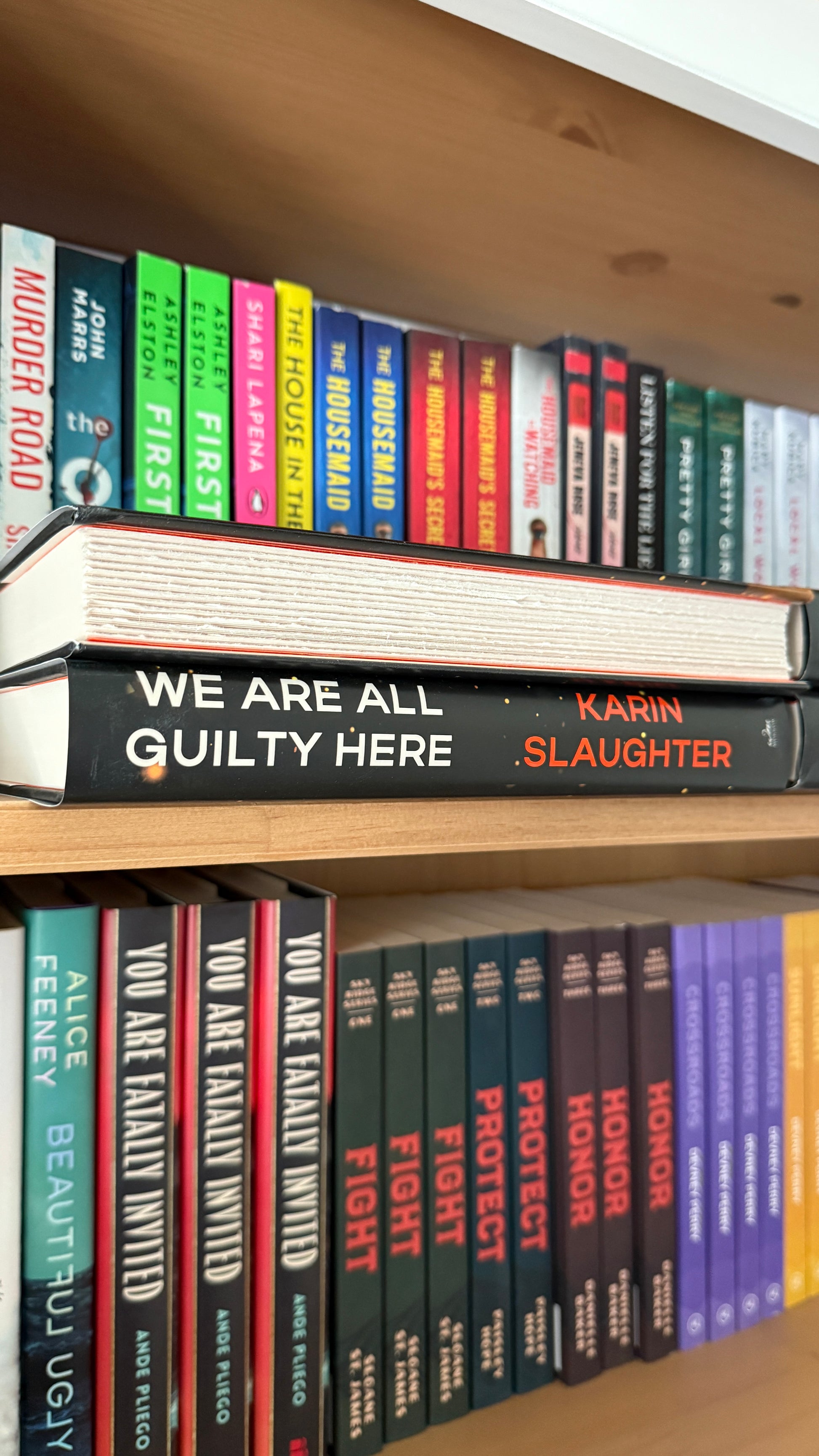 Bookshelf with books, including 'We Are All Guilty Here' by Karin Slaughter, arranged vertically.