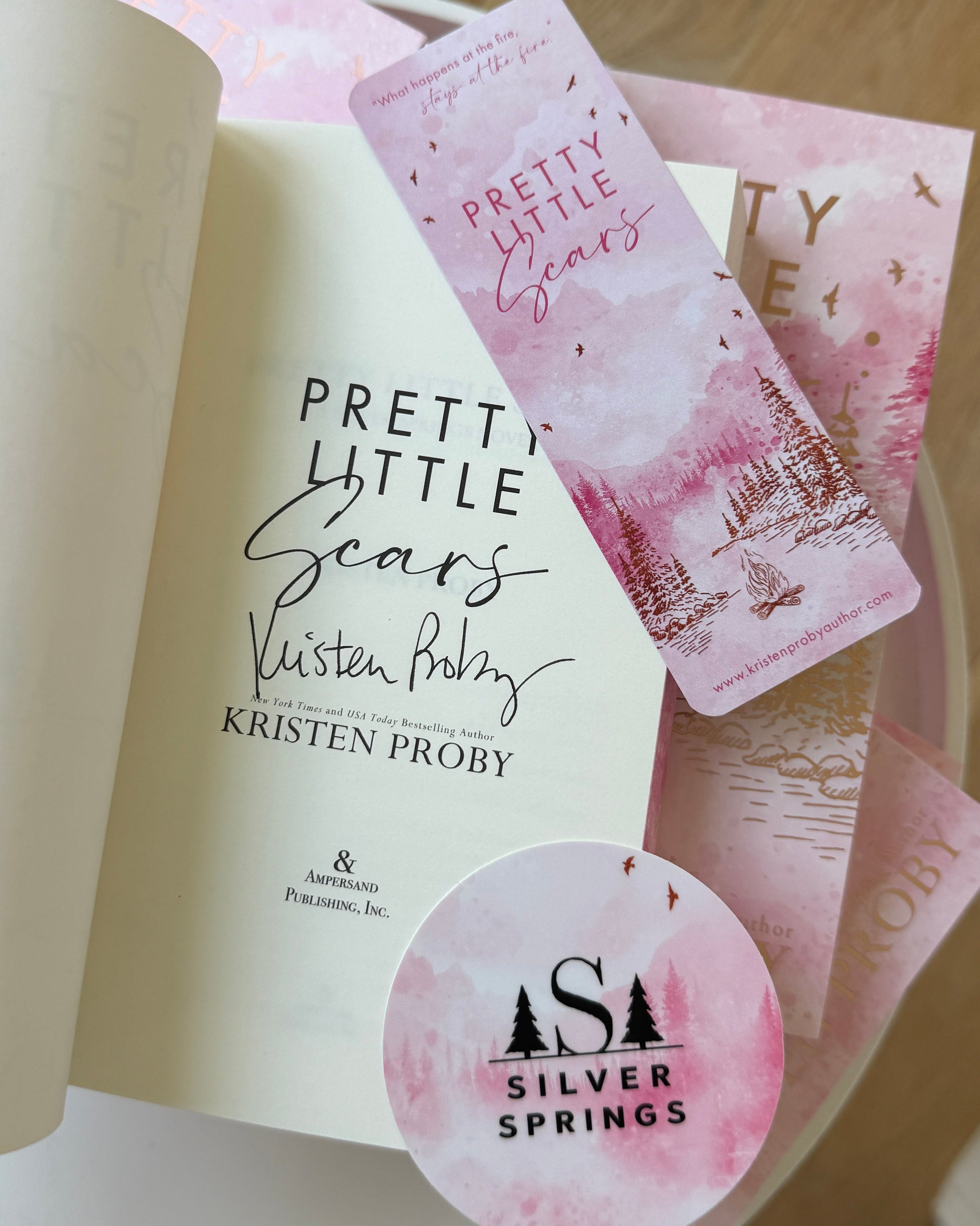 Book titled 'Pretty Little Secrets' by Kristen Proby with a pink bookmark and 'Silver Springs' sticker on a wooden surface.