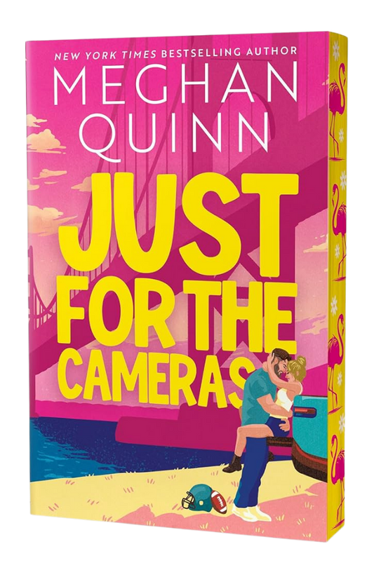 Book cover of 'Just for the Cameras' by Meghan Quinn with a colorful design and couple on a boat.