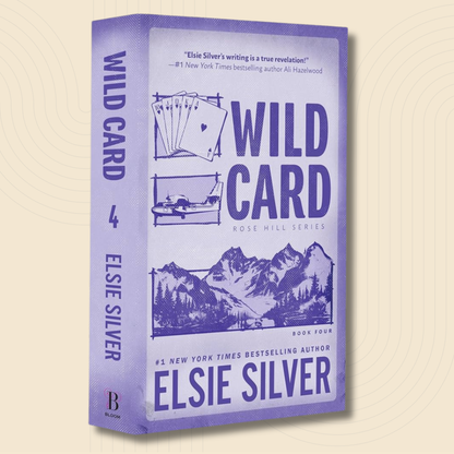 The book 'Wild Card' by Elsie Silver, shown as a 3D box mockup on a light beige background with a subtle circular pattern. The cover and spine are lavender purple with dark purple text and illustrations of playing cards and a mountain landscape.