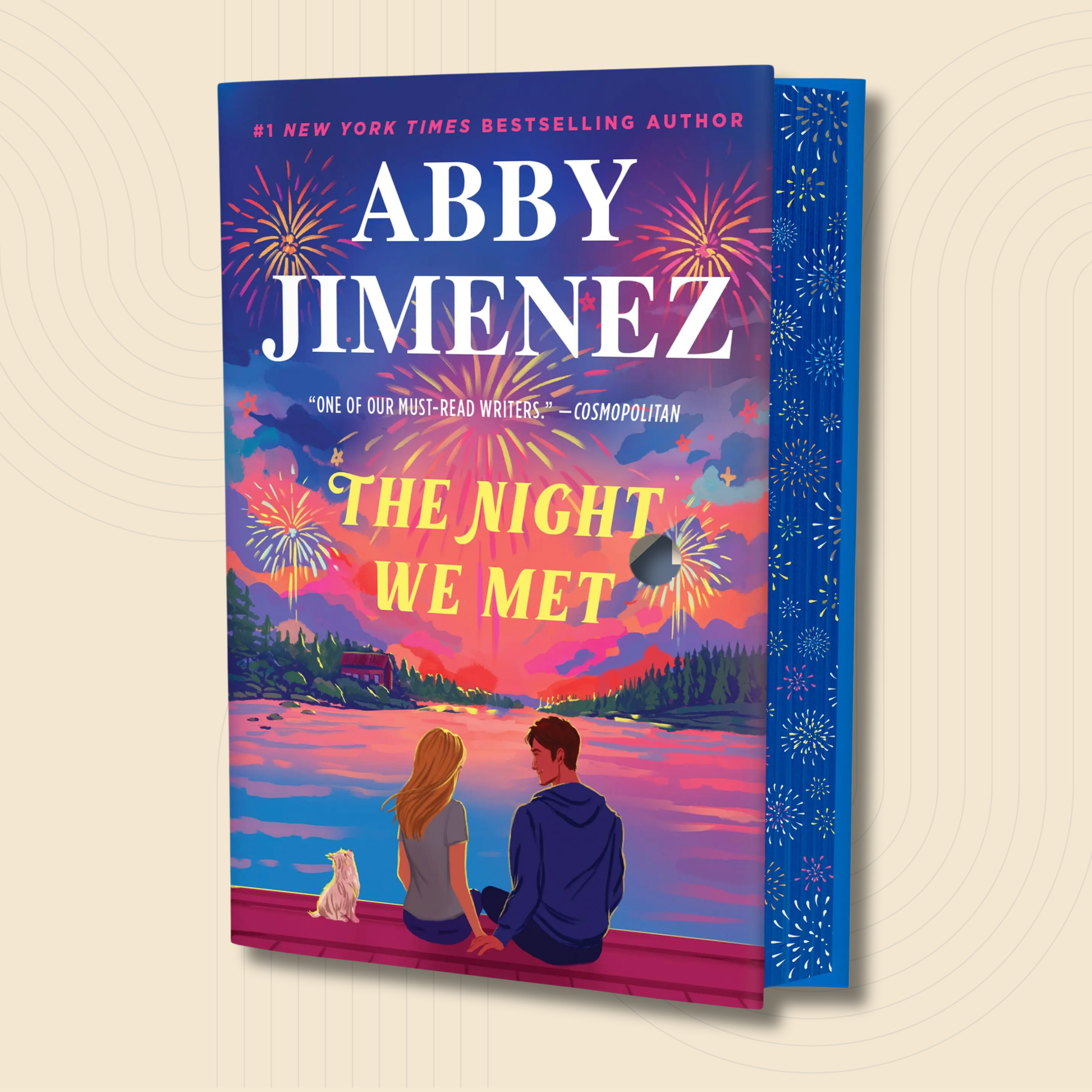 The Night We Met paperback book by Abby Jimenez, featuring a vibrant, colorful cover illustration of a couple and a dog sitting on a dock at sunset, shown against a light beige background with a subtle concentric circle pattern.