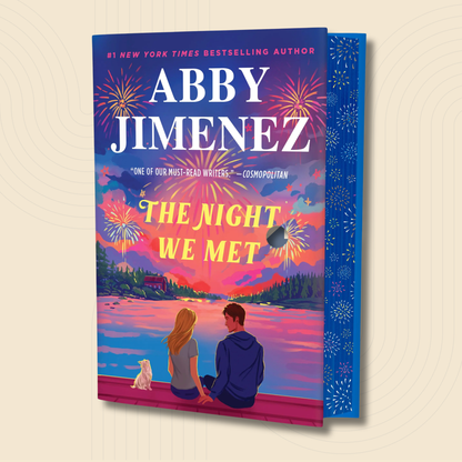 The Night We Met paperback book by Abby Jimenez, featuring a vibrant, colorful cover illustration of a couple and a dog sitting on a dock at sunset, shown against a light beige background with a subtle concentric circle pattern.