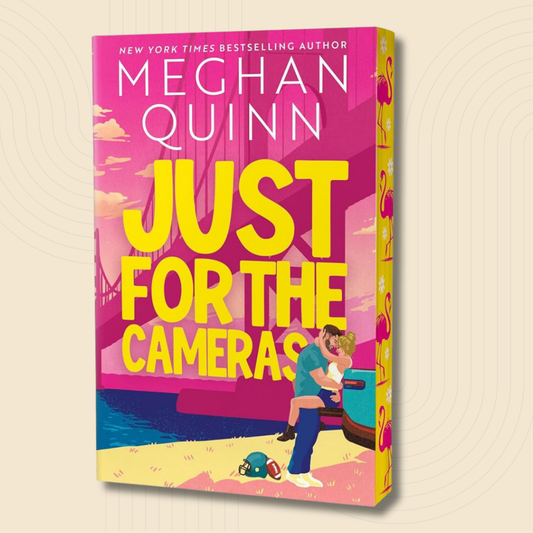 Book cover for 'Just for the Cameras' by Meghan Quinn, featuring a bright pink and yellow design with an illustration of a couple embracing by a car on a beach.